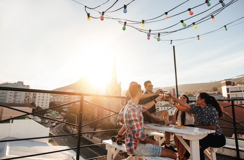 Outdoor shot of young people toasting drinks at a rooftop party. Young friends hanging out with drin...