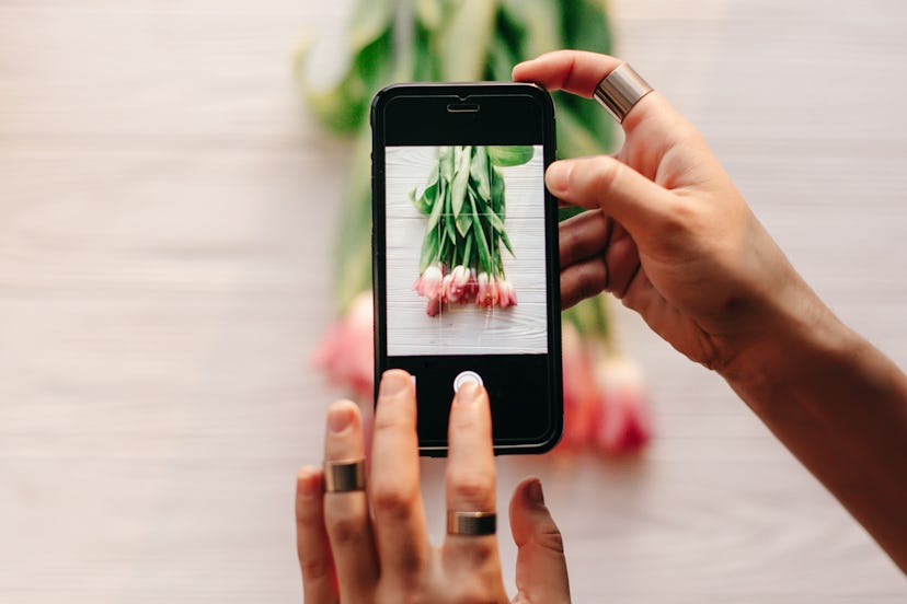 instagram photographer blogging workshop concept. hand holding phone and taking photo of stylish flo...