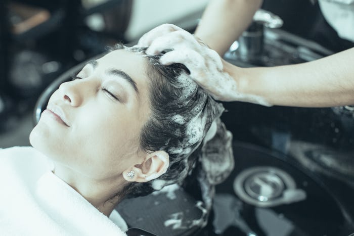 Hands of hairdresser washing hair of enjoying young Latin American woman with shampoo