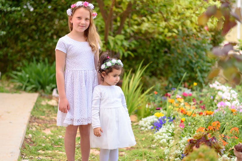 Two happy multiracial children with white dress and flower wreath playing outdoors. Kids having fun ...