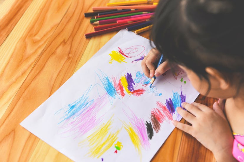 Girl painting on paper sheet with colour pencils on the wooden table at home / child kid doing drawi...