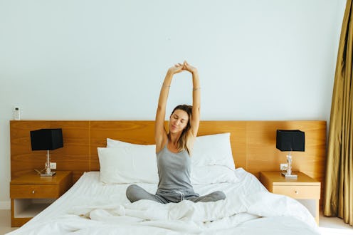 Woman waking up and stretching on bed in luxury hotel room in the morning. Sleeping well on comfy ma...