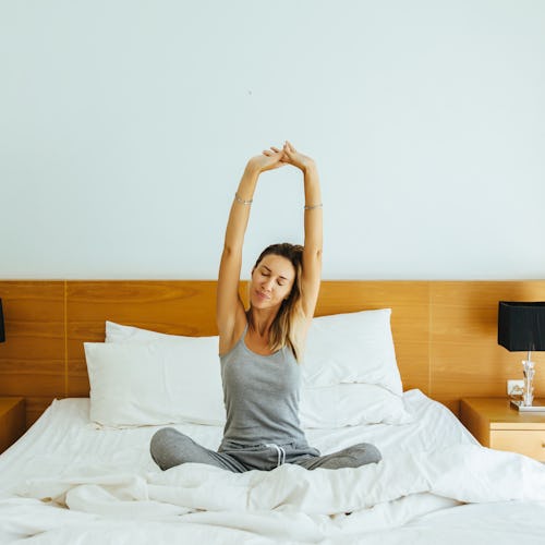 Woman waking up and stretching on bed in luxury hotel room in the morning. Sleeping well on comfy ma...