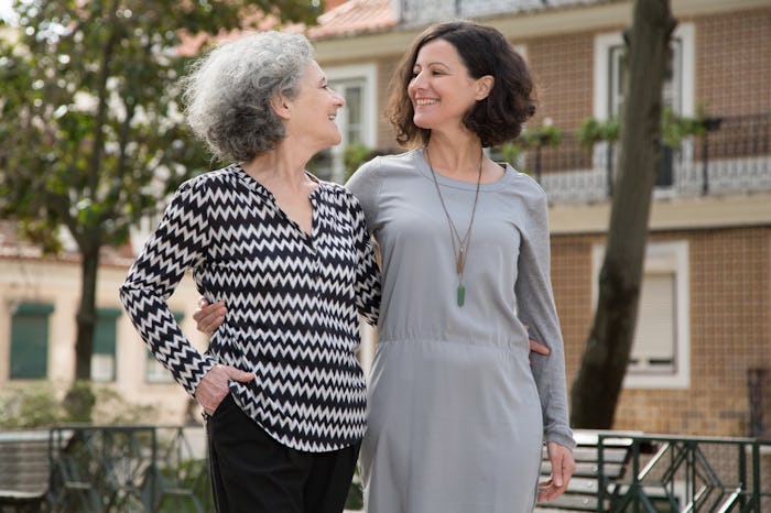 Cheerful smiling mother and daughter walking around uptown old district. Young and senior women hugg...
