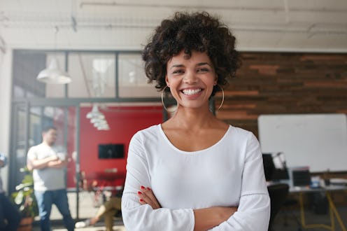 Smiling young woman standing with her arms crossed and looking at camera. She is standing in a moder...