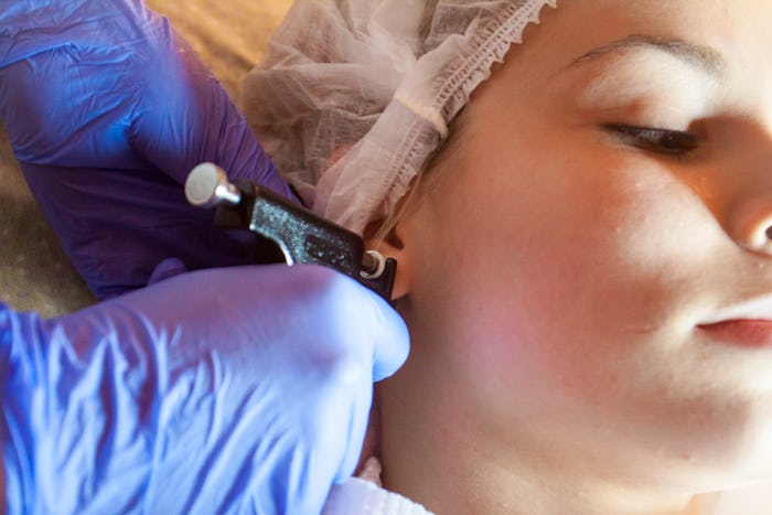 piercing ears to a girl in a spa salon by a doctor using a special device machine