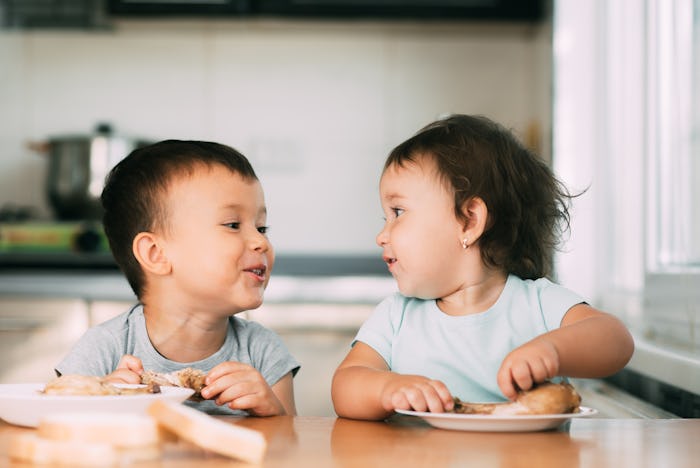 Kids boy and girl , brother and sister in the kitchen having fun and eating chicken with appetite is...