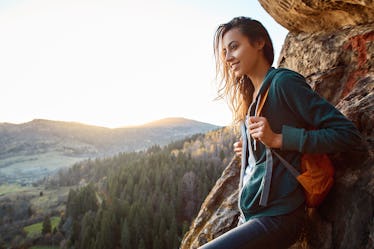 Young hiker wearing a backpack on a mountain before posting a pic on Instagram with hiking puns, mou...