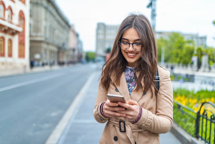 Texting on the phone. Happy young woman with her mobile on the street. Attractive young woman textin...