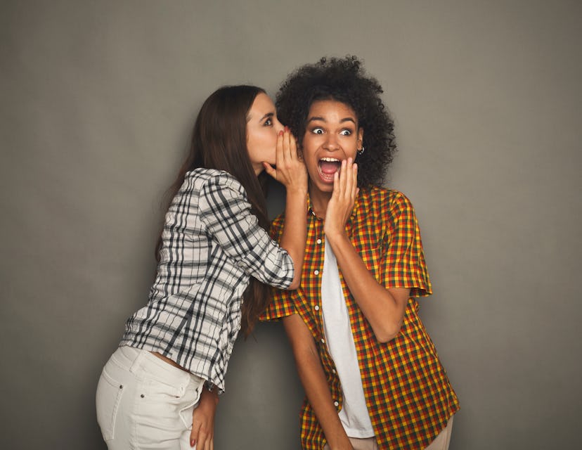 Young woman telling her girlfriend some secret. Two women gossiping. Excited emotional girl whisperi...