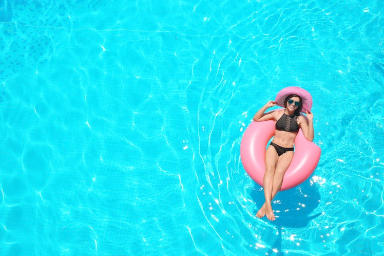 Beautiful young woman with inflatable ring relaxing in blue swimming pool