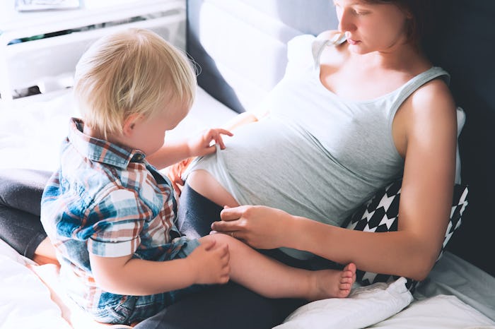 Pregnant mother and son are talking and spending time together in bed at home. Little child boy look...