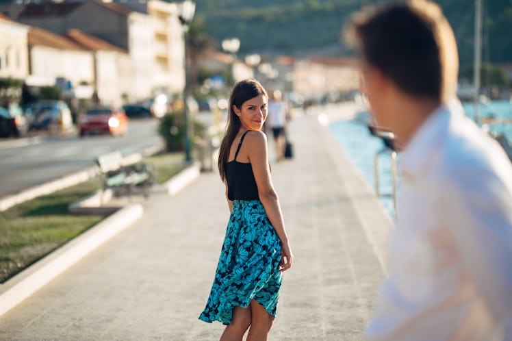 Young attractive woman flirting with a man on the street.Flirty smiling woman looking back on a hand...