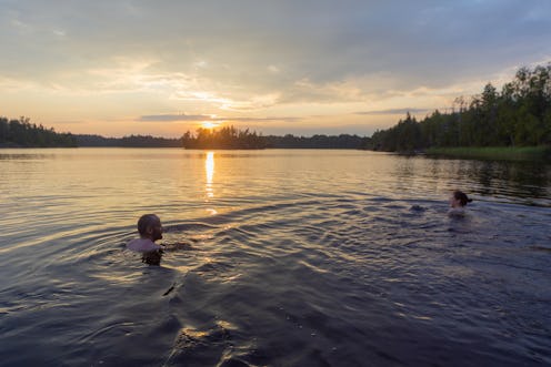 man and woman are swimming in the lake at sunset