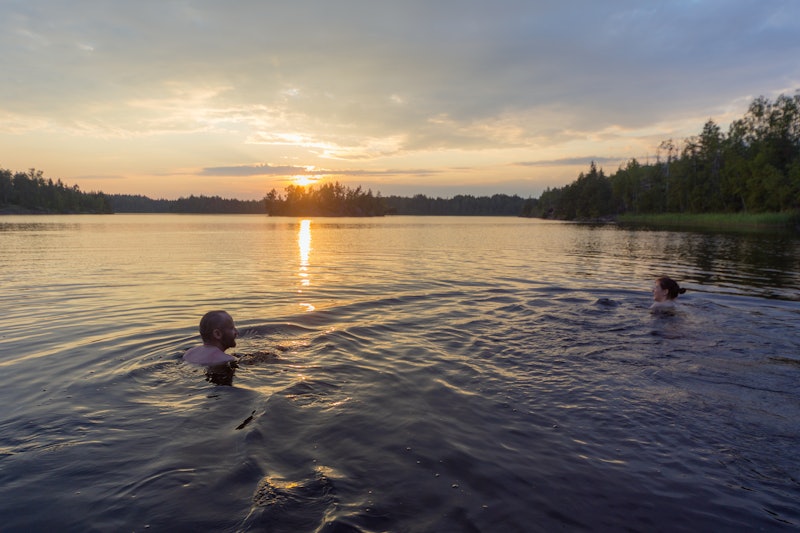 man and woman are swimming in the lake at sunset