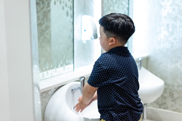 A fat boy washing hands in the kid restroom.