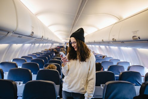Beautiful girl in glasses and hat sitting on the seat in the airplane and making selfie. Traveler sm...