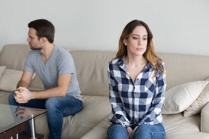 Offended husband and wife sit separately on couch avoid talking or looking at each other, millennial...