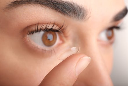 Young woman putting contact lens in her eye, close up view. Medicine and vision concept