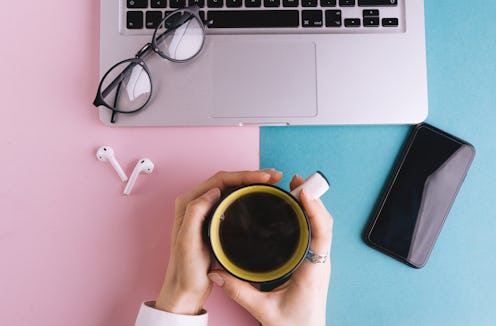 Top view of woman hand holding cup with cofee, flat lay on pin blue workspace table with laptop, gla...