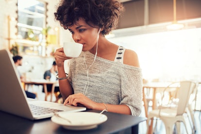 Portrait of young african woman drinking coffee and using laptop at a cafe.