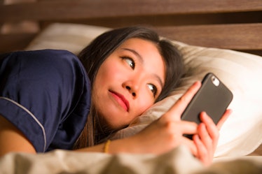 young beautiful and happy Asian Korean woman in pajamas using mobile phone social media texting with...