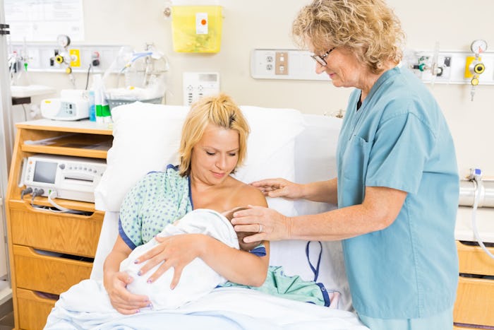 Mature nurse helping woman in breast feeding newborn baby in hospital room