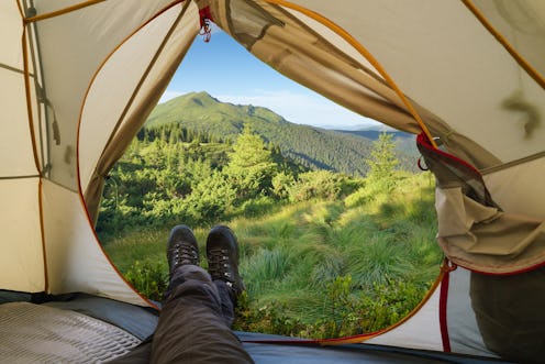 Camping in the mountains. Summer hike. View from a tourist tent on a peak. Guy in trekking boots