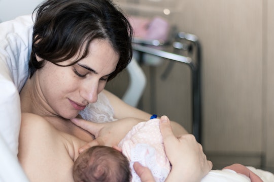 New mother carefully breastfeeds her newborn baby girl in hospital bed.