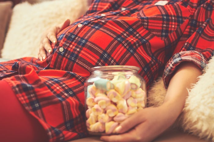 Pregnant woman eating candy. Focus on belly.