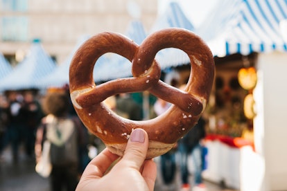 A girl or a young woman is holding a traditional German pretzel in the street. Oktoberfest festival ...