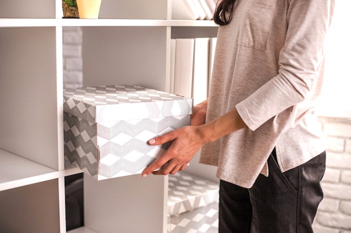 Woman put a cardboard box on shelf. Concept of organization of work space.