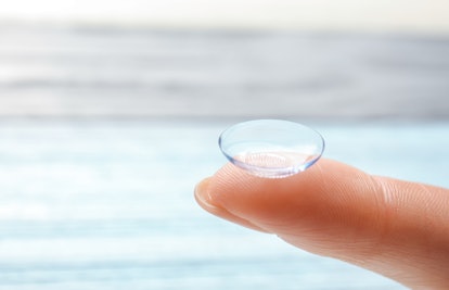 Female finger with contact lens on blurred background