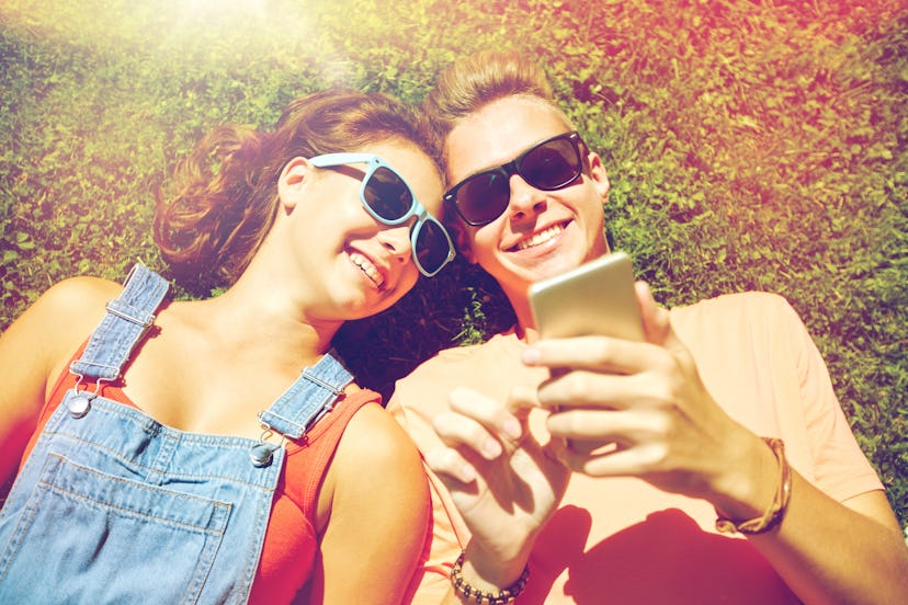 love and people concept - happy teenage couple in sunglasses with smartphone lying on grass at summe...