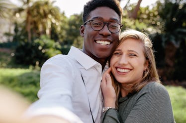 Beautiful interracial couple making a selfie outdoors. African man with caucasian woman taking a sel...