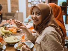 beautiful asian muslim woman smiling to camera while having dinner together with family