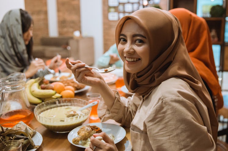 beautiful asian muslim woman smiling to camera while having dinner together with family