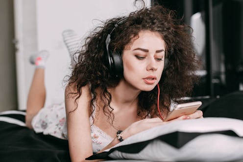 Curly brunette lies on bed listening to the music on iPhone