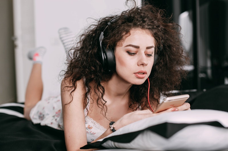 Curly brunette lies on bed listening to the music on iPhone