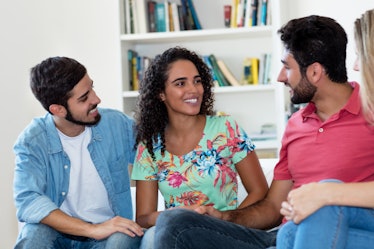 Latin american man and woman talking with group of friends indoors at home