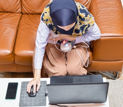 Busy young modern mother working with laptop while using automatically electric breast pump feeding ...