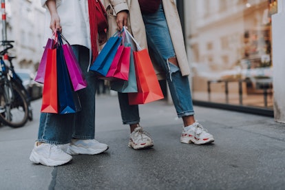Look what we bought. Close up of two girl in jeans and sneakers holding colorful shopping bags