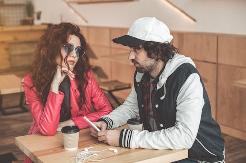 Young man and woman are looking at each other with seriousness while sitting in cafeteria. Guy is ho...