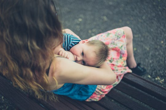 A young mother is breastfeeding her baby on a park bench