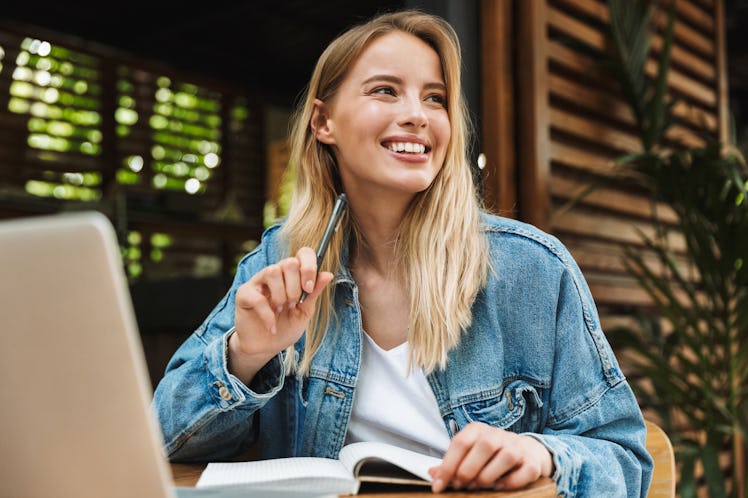 Image of amazing happy young woman student posing outdoors in cafe using laptop computer writing not...