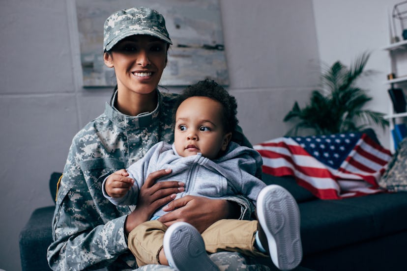 smiling mother in military uniform with her little son at home, with american flag on background