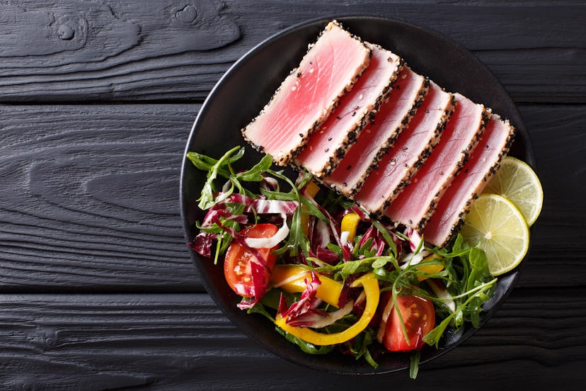 Close up of rare seared Ahi tuna slices with fresh vegetable salad on a plate. Top view from above h...