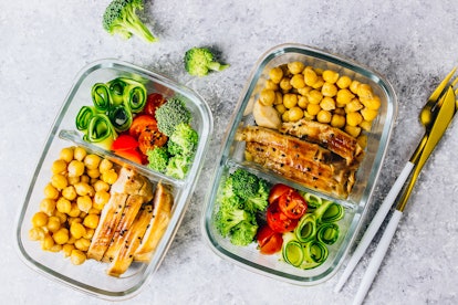 Healthy meal prep containers with chickpeas, chicken, tomatoes, cucumbers, avocados and broccoli. To...