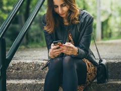 Woman looking at cell phone with worried expression on face.