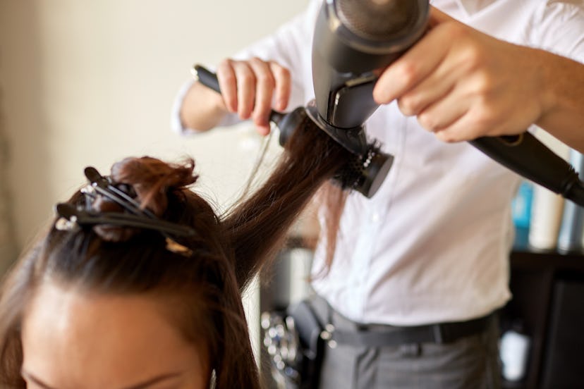 beauty, hairstyle, blow-dry and people concept - close up of young woman and hairdresser with fan an...